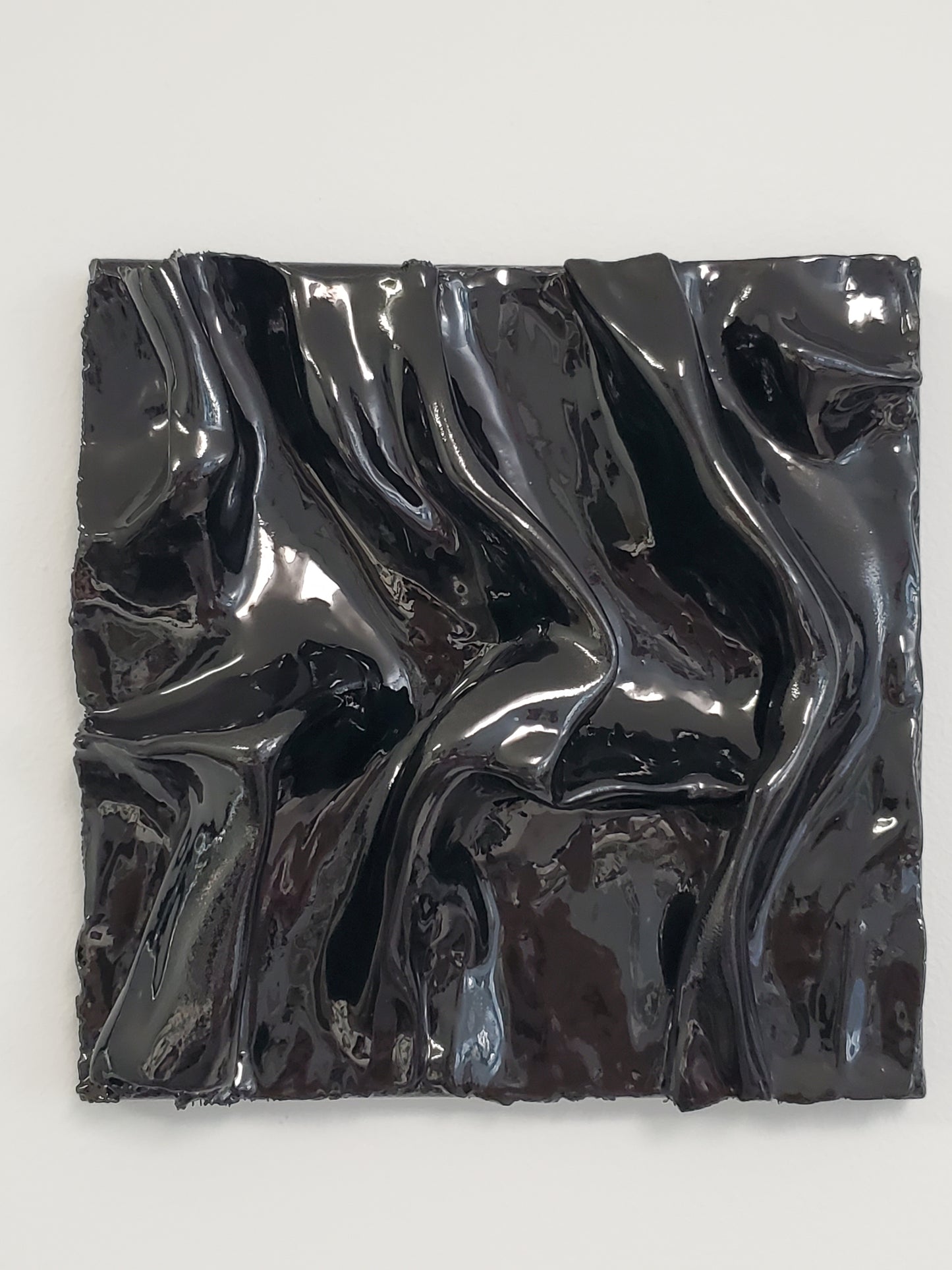 A black, textured artwork made of plaster with a clear glaze to give it a silky fabric or wet molded glass look