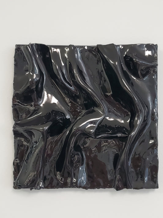 A black, textured artwork made of plaster with a clear glaze to give it a silky fabric or wet molded glass look