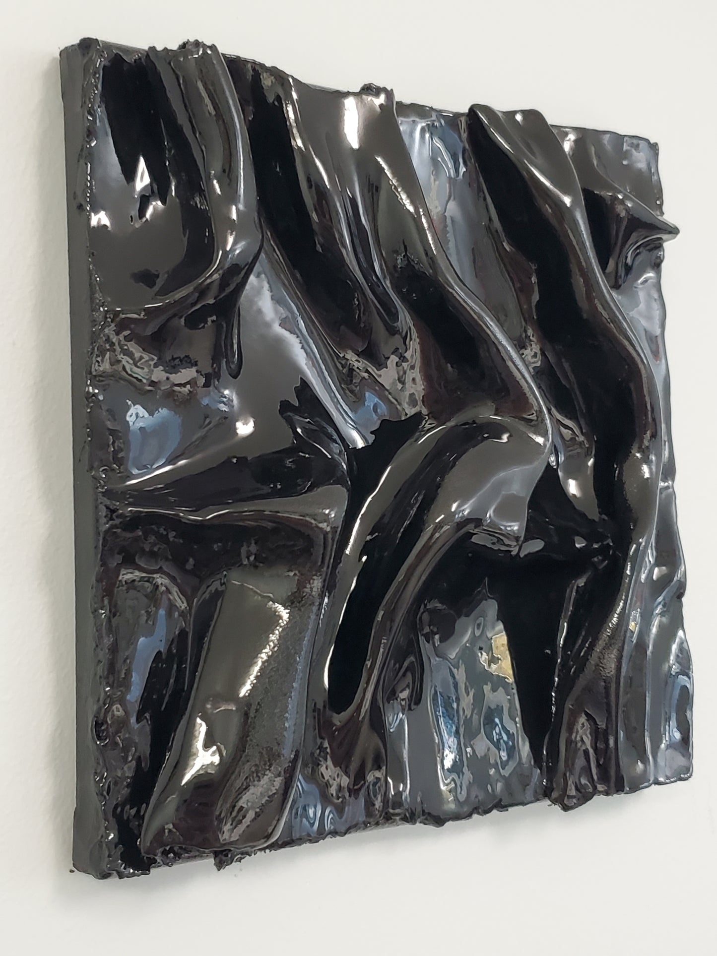 side view of a black, textured artwork made of plaster with a clear glaze to give it a silky fabric or wet molded glass look