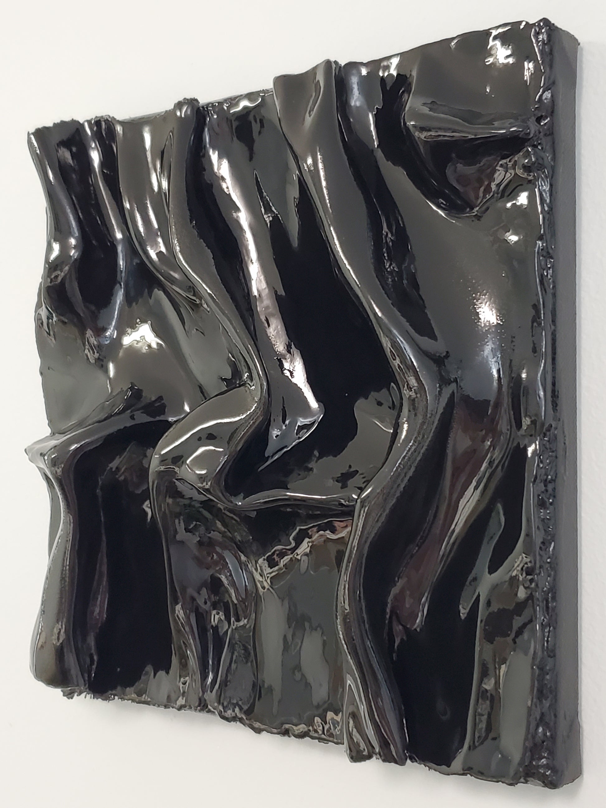 right angled view of a black, textured artwork made of plaster with a clear glaze to give it a silky fabric or wet molded glass look