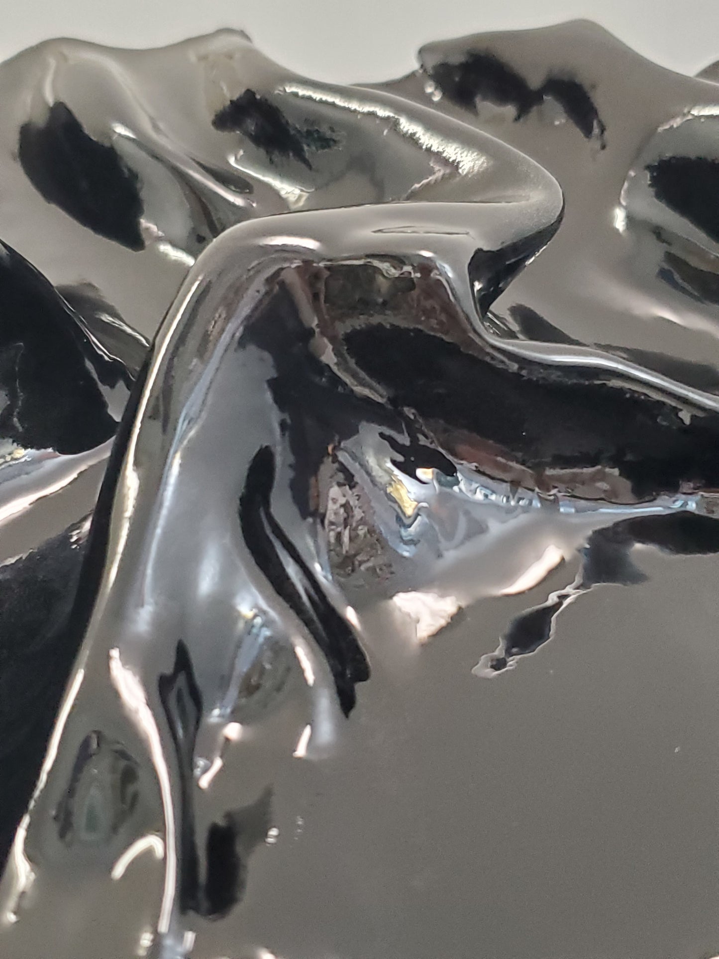 close up of A black, textured artwork made of plaster with a clear glaze to give it a silky fabric or wet molded glass look