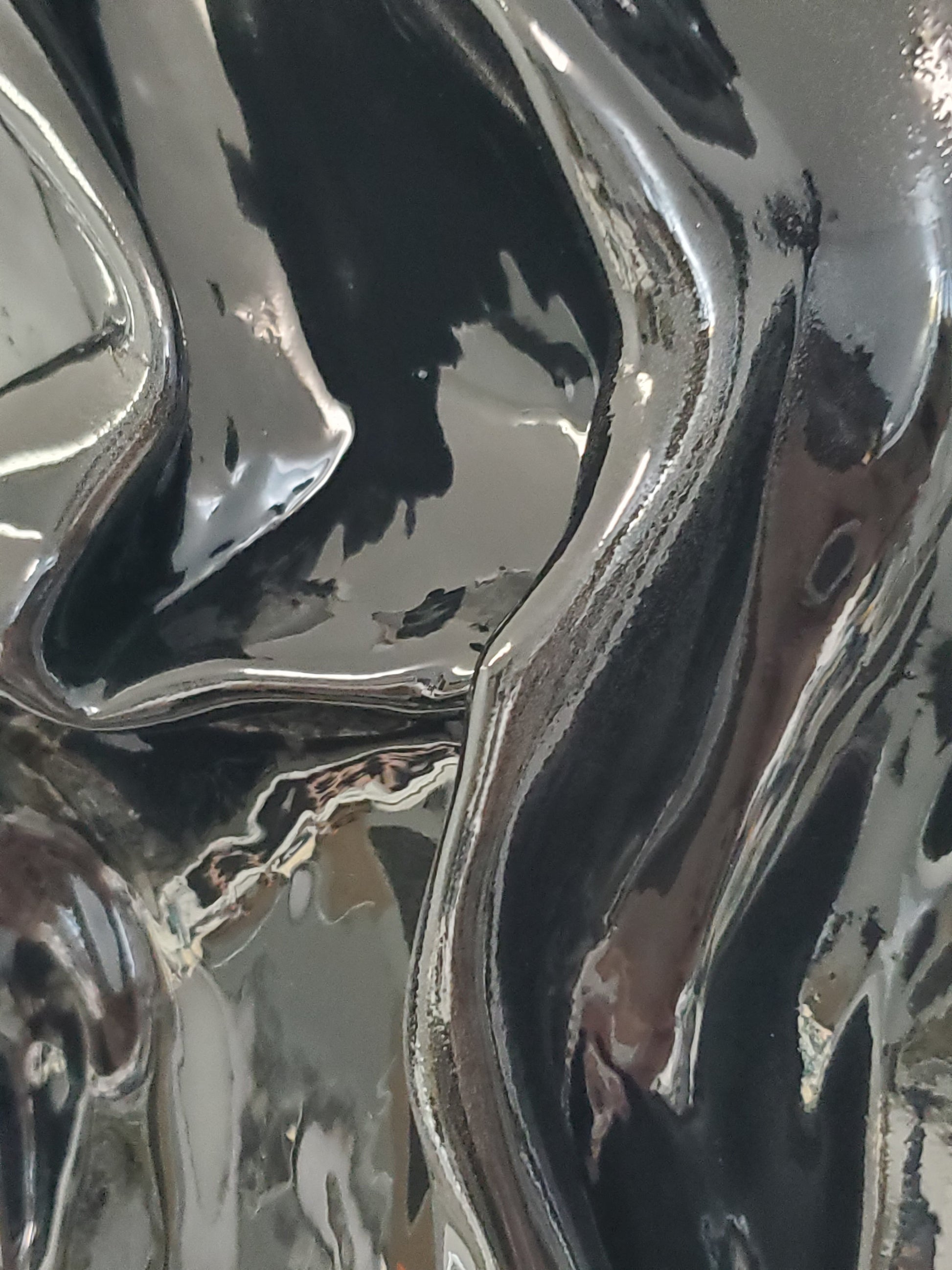 close up of A black, textured artwork made of plaster with a clear glaze to give it a silky fabric or wet molded glass look