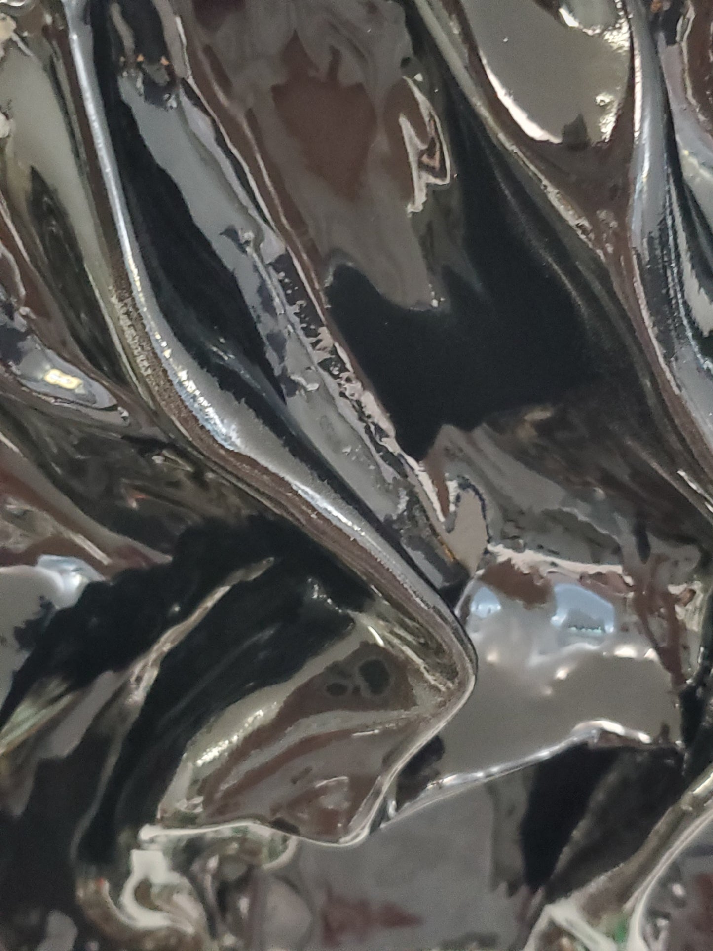 close up of A black, textured artwork made of plaster with a clear glaze to give it a silky fabric or wet molded glass look
