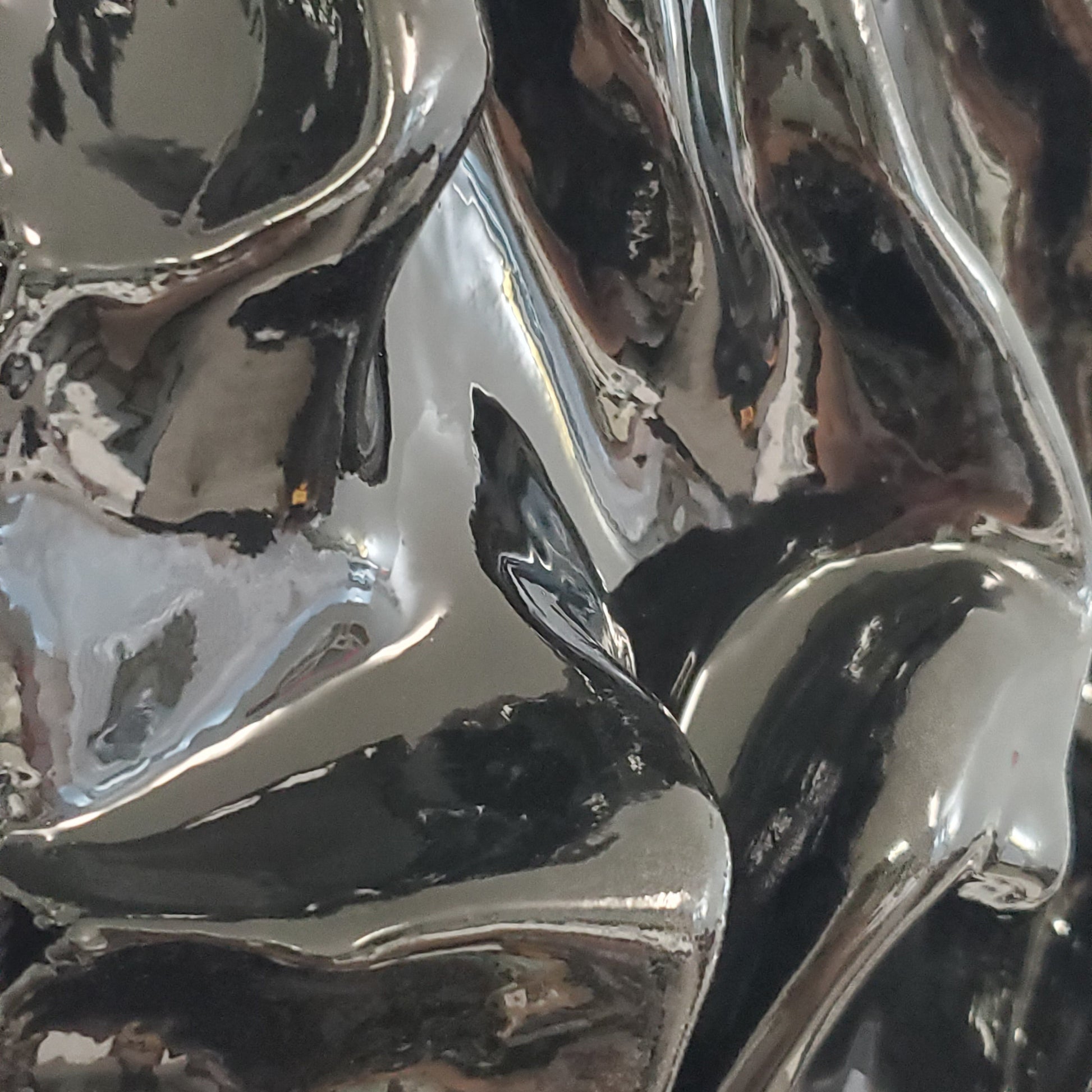 Close-up of reflective surface with wavy patterns. A black, textured artwork made of plaster with a clear glaze to give it a silky fabric or wet molded glass or metallic look