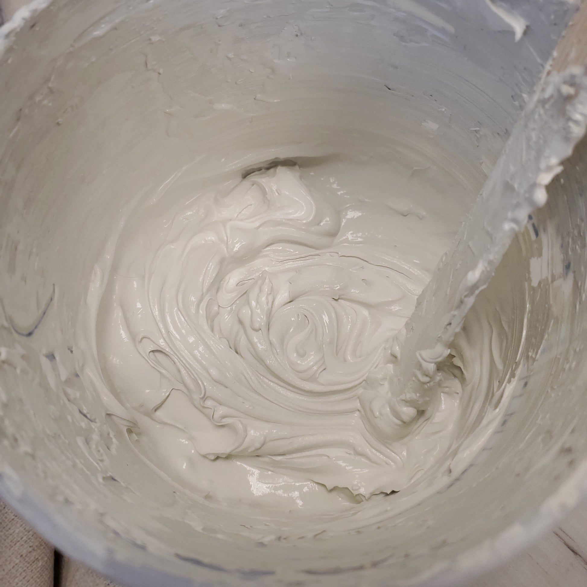 Close-up of drywall mud and neutral paint a container with a paint stick