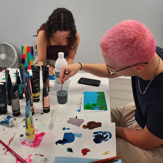 Two people sitting at a table with art supplies and a colorful painting.